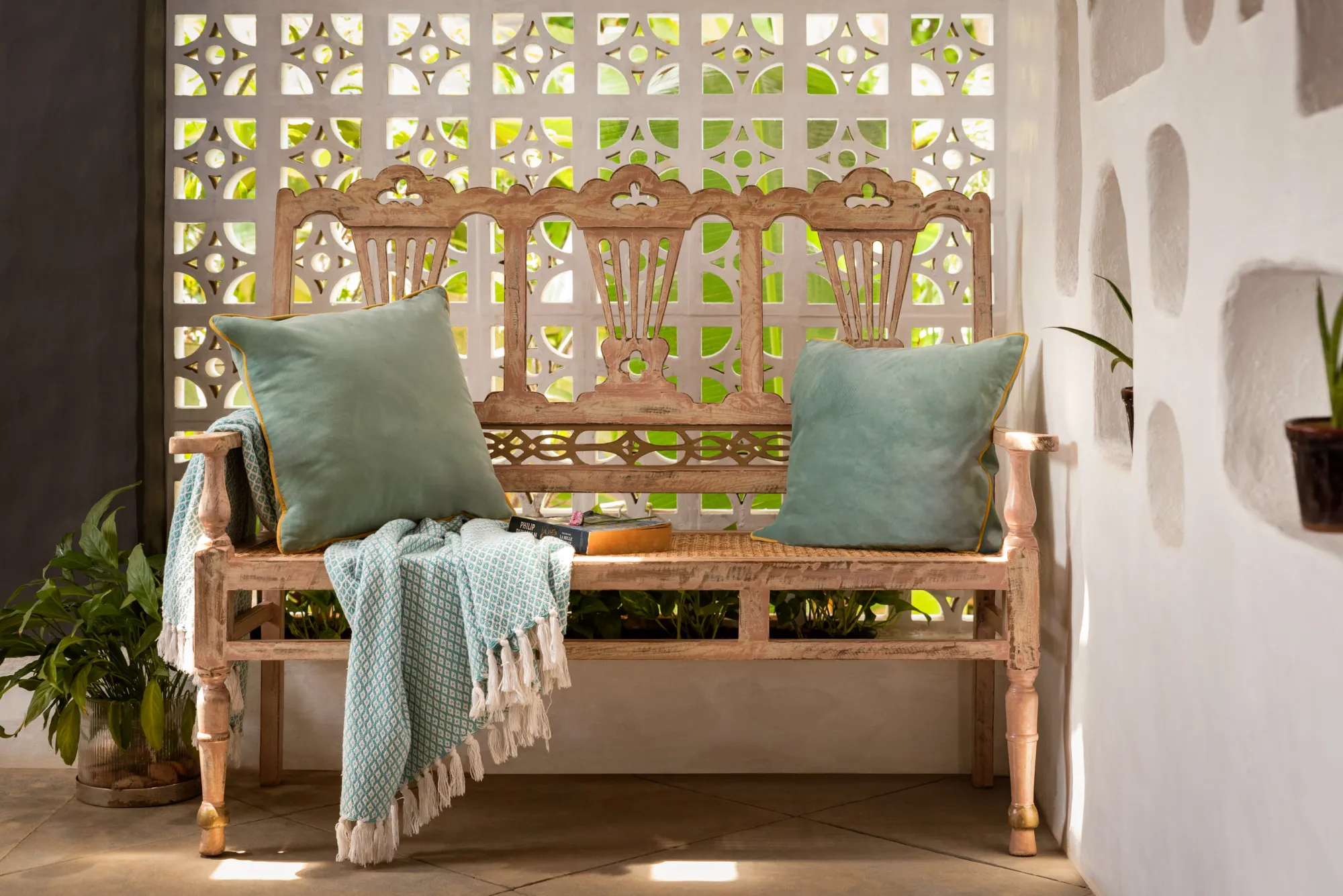 A carved wooden bench with sage cushions in front of a white jaali screen